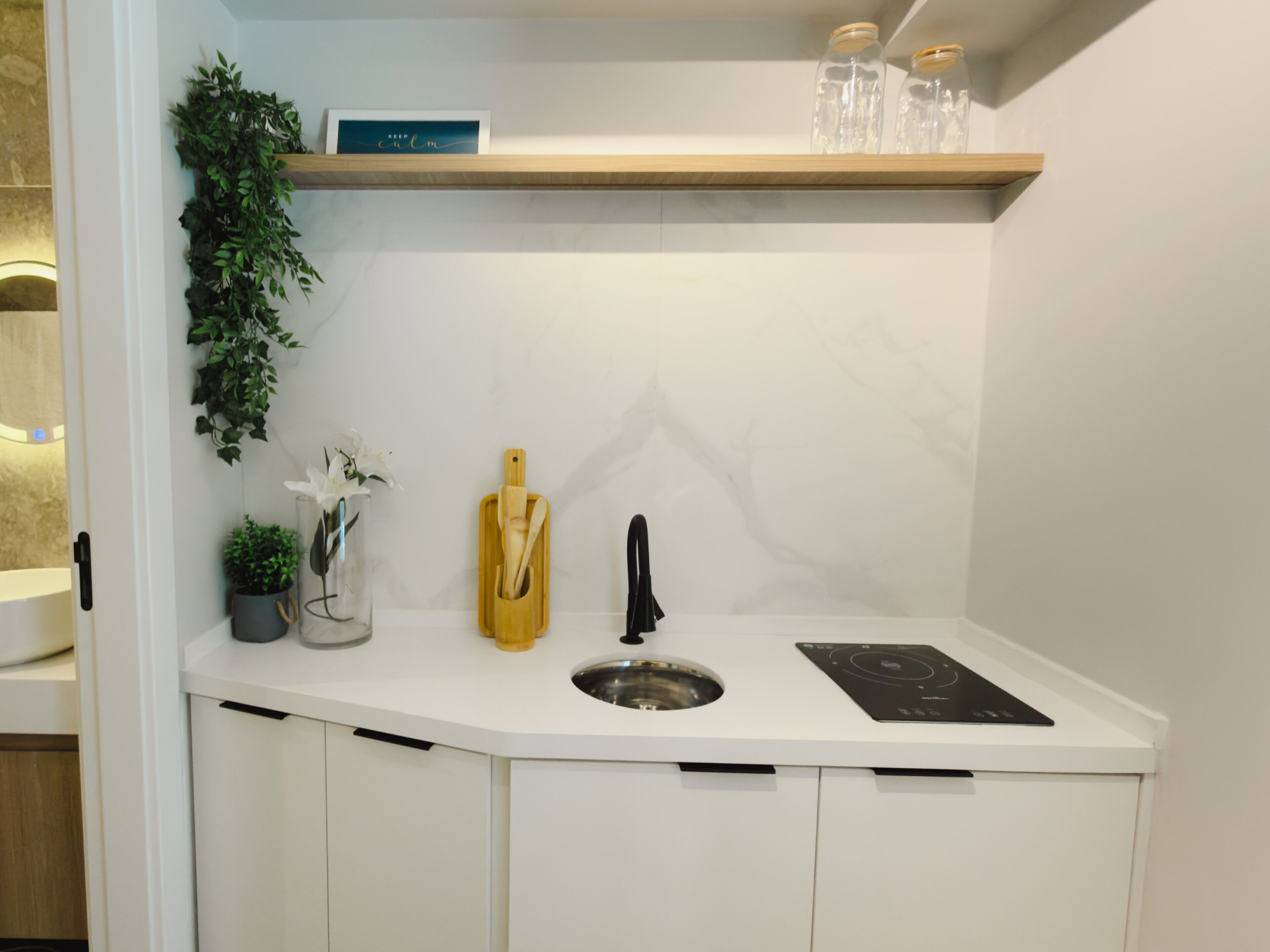Una cocina moderna con armarios blancos, un lavamanos integrado, un grifo negro y un organizador de utensilios de madera.