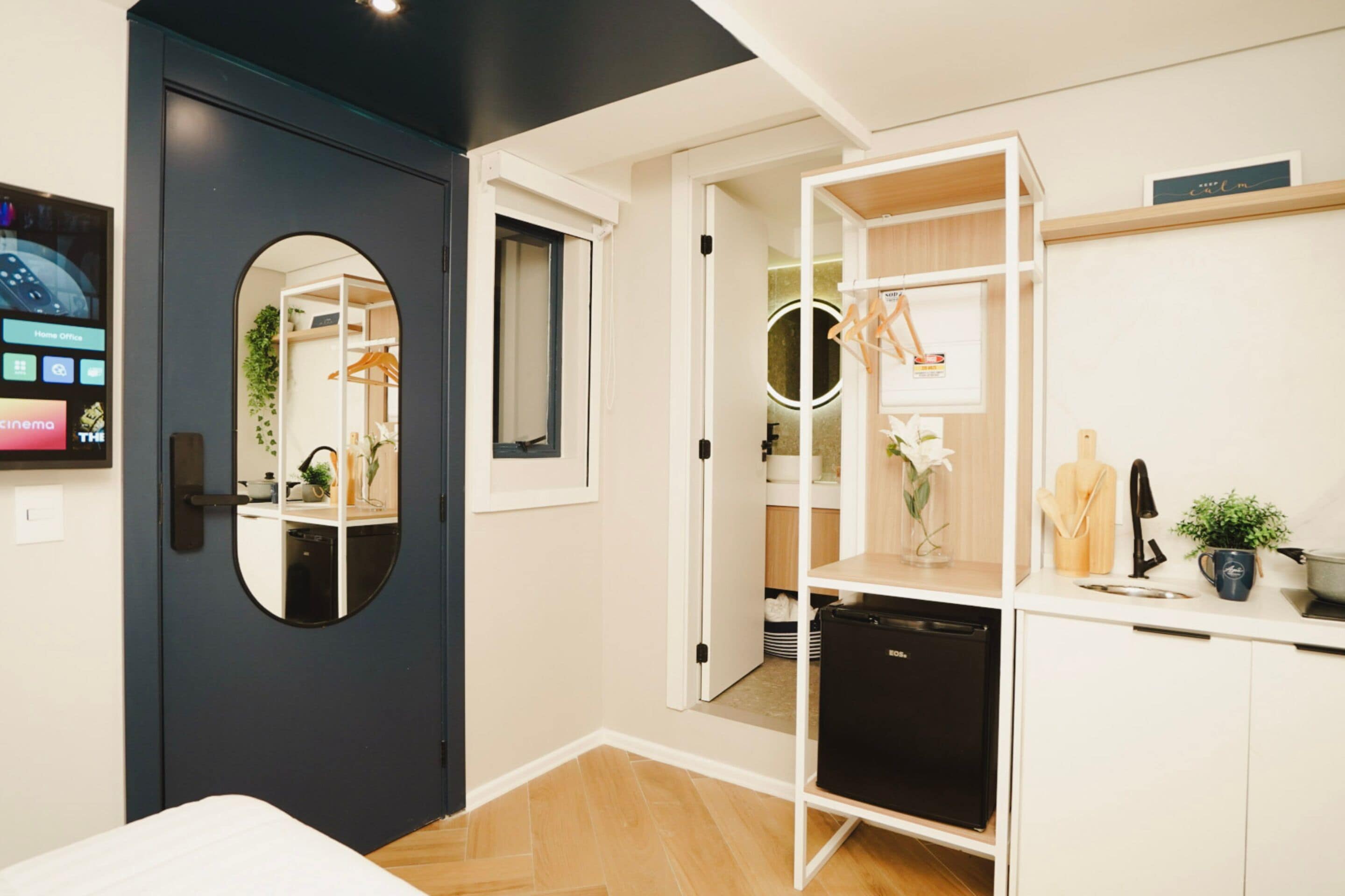 Une chambre à coucher de taille modeste, avec une porte sombre, une petite table de chevet, un miroir et une armoire agrémentée d’un miroir rond.