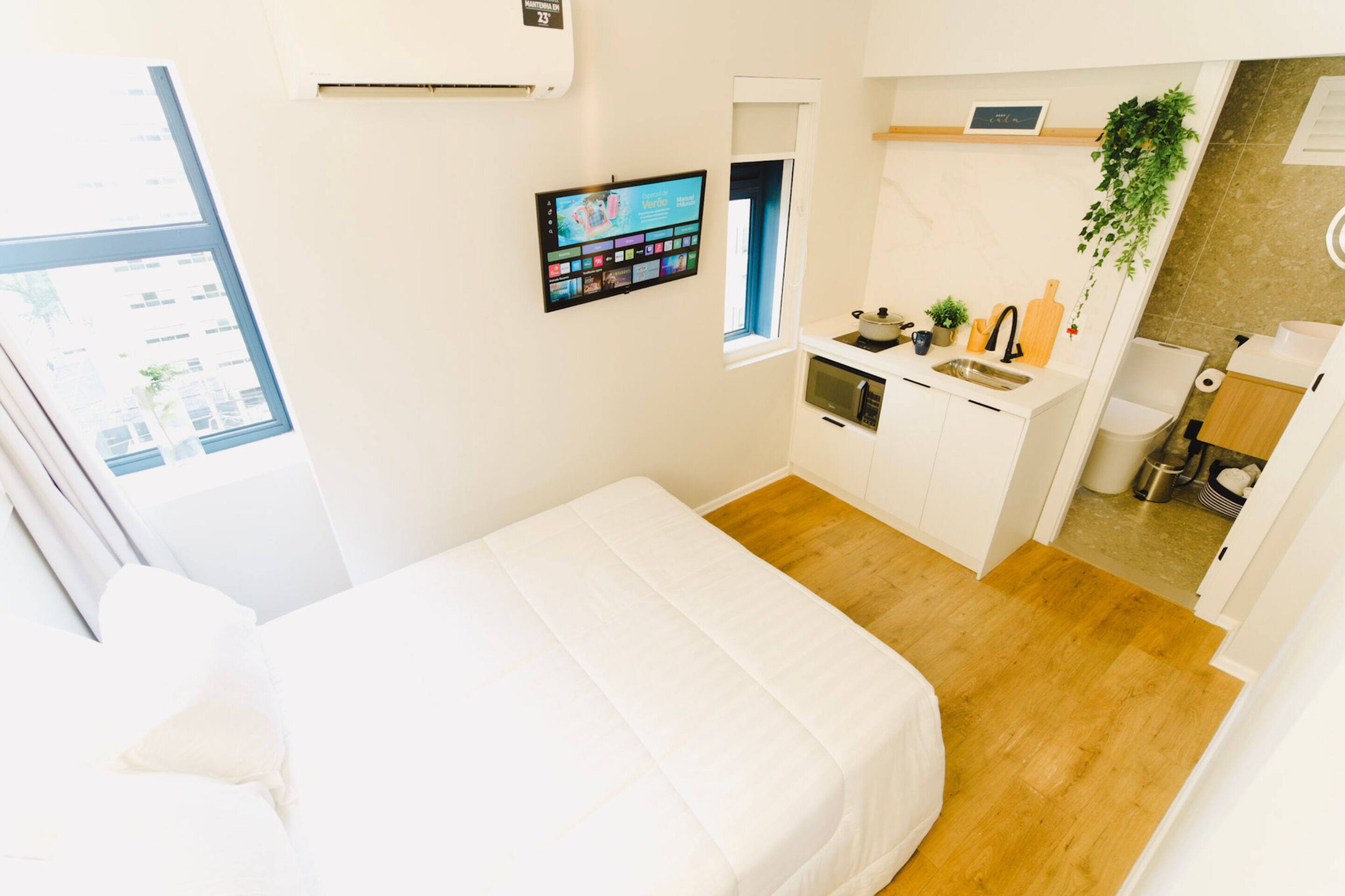Una camera d'albergo compatta con un letto, angolo cottura, finestra e televisore a parete.