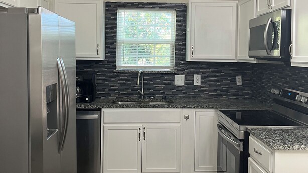 Una cocina moderna con armarios blancos, un refrigerador de acero inoxidable, un microondas y un respingo de azulejos negros.