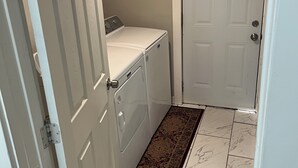Un lavadero con una puerta blanca, una lavadora y una alfombra estampada en el suelo.