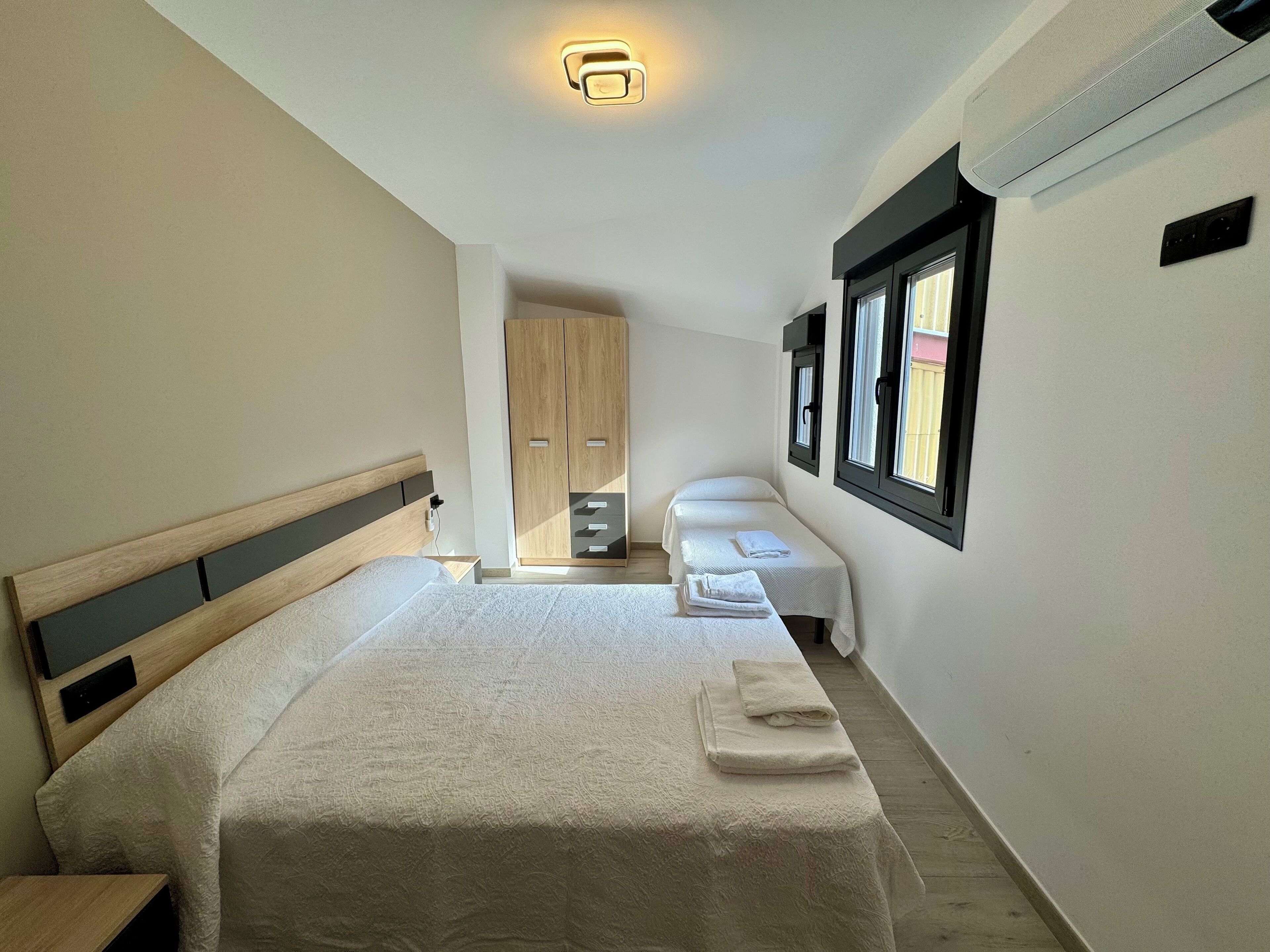 A bedroom with a large bed, a smaller bed, a wardrobe, and a window with blinds.