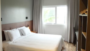 Una habitación de hotel con cama, ventana con cortinas, mesita de noche y armario.