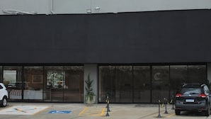 Un edificio con ventanas grandes, un estacionamiento con espacios reservados para discapacitados y un coche negro estacionado al frente.