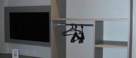 A room with a bed, a TV mounted on the wall, a small fridge, and a wardrobe with shelves and hanging space.