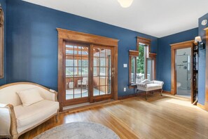 Une pièce avec un mur bleu, un plancher en bois, un canapé blanc, un tapis rond et une porte en verre donnant sur un espace extérieur.