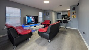 Una sala moderna con un televisor de pantalla plana, dos sofás de cuero rojo y negro, una mesa de centro y una cocina al fondo.