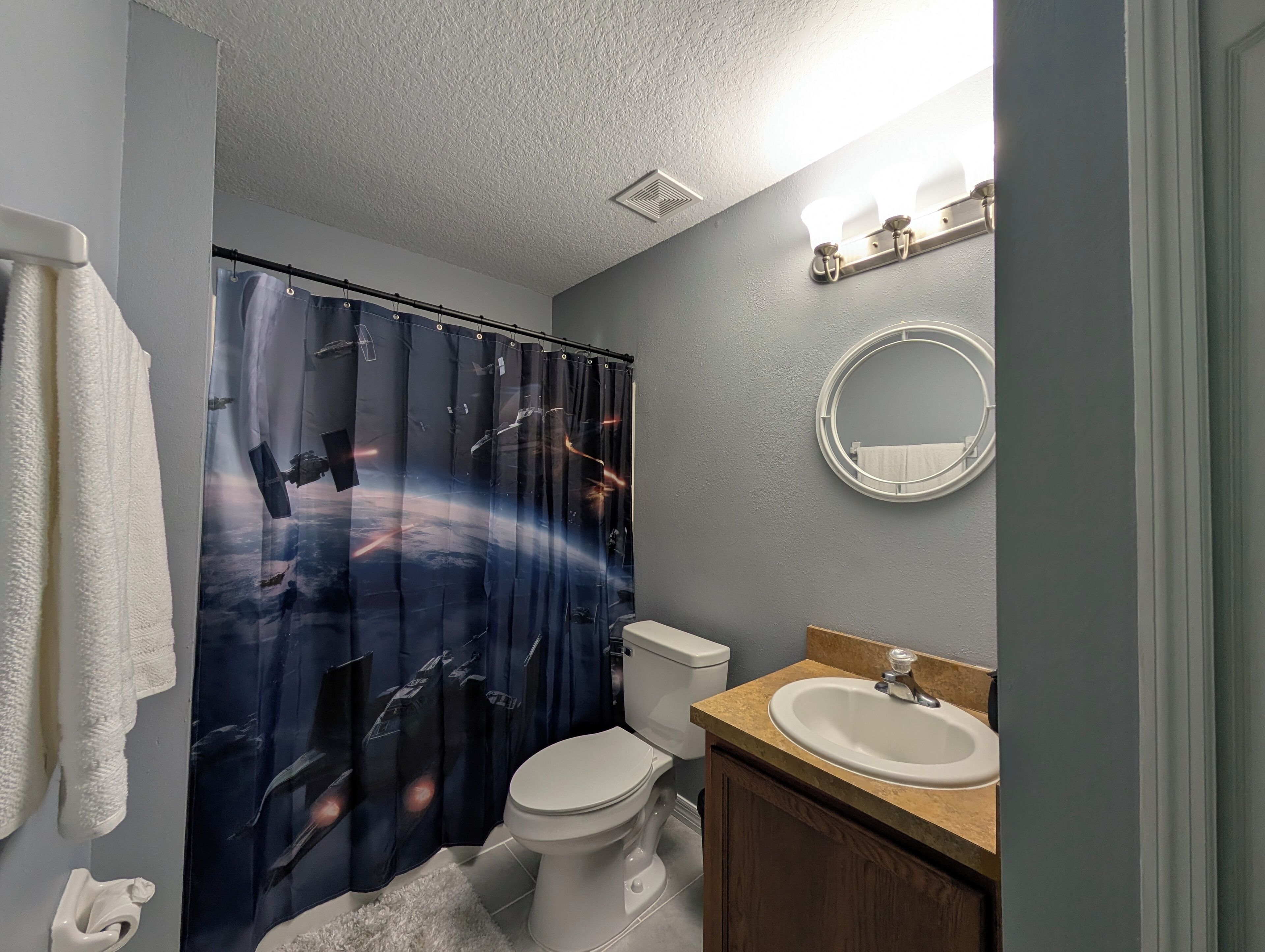 A bathroom with a space-themed shower curtain, a toilet, a sink, and a mirror.