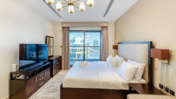 Ein modernes Hotelzimmer mit einem großen Bett, einem Fernseher, einem Schminktisch und Blick auf die Stadt.
