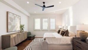A modern bedroom with a bed, bedside tables, a desk, a chair, a ceiling fan, and a window with blinds. - Luxury 3-bedroom house near the pier in San Clemente (San Clemente)