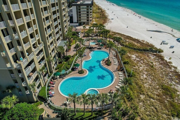 A hotel with a large swimming pool, a beach, and a high-rise building.
