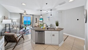 A modern kitchen with a dishwasher, a dining area with a table and chairs, and a view of the ocean.