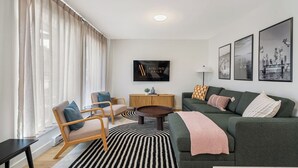 A modern living room with a sofa, armchair, and coffee table, a television, and framed pictures on the wall. - Summit Stay | Ground Floor | Central | AC | Pets (Invermere)