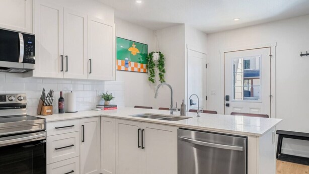 A modern kitchen with white cabinetry, stainless steel appliances, and a large window. - Summit Stay | Ground Floor | Central | AC | Pets (Invermere)