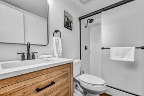 Ein modernes Badezimmer mit einem weißen Waschbecken, einem Holz-Badmöbel, einer Toilette, einer Dusche mit Glastür und einem Handtuchhalter.