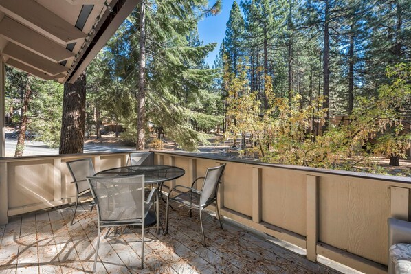 Eine überdachte Terrasse mit Tisch und Stühlen, umgeben von hohen Bäumen und Blick auf ein bewaldetes Gebiet.