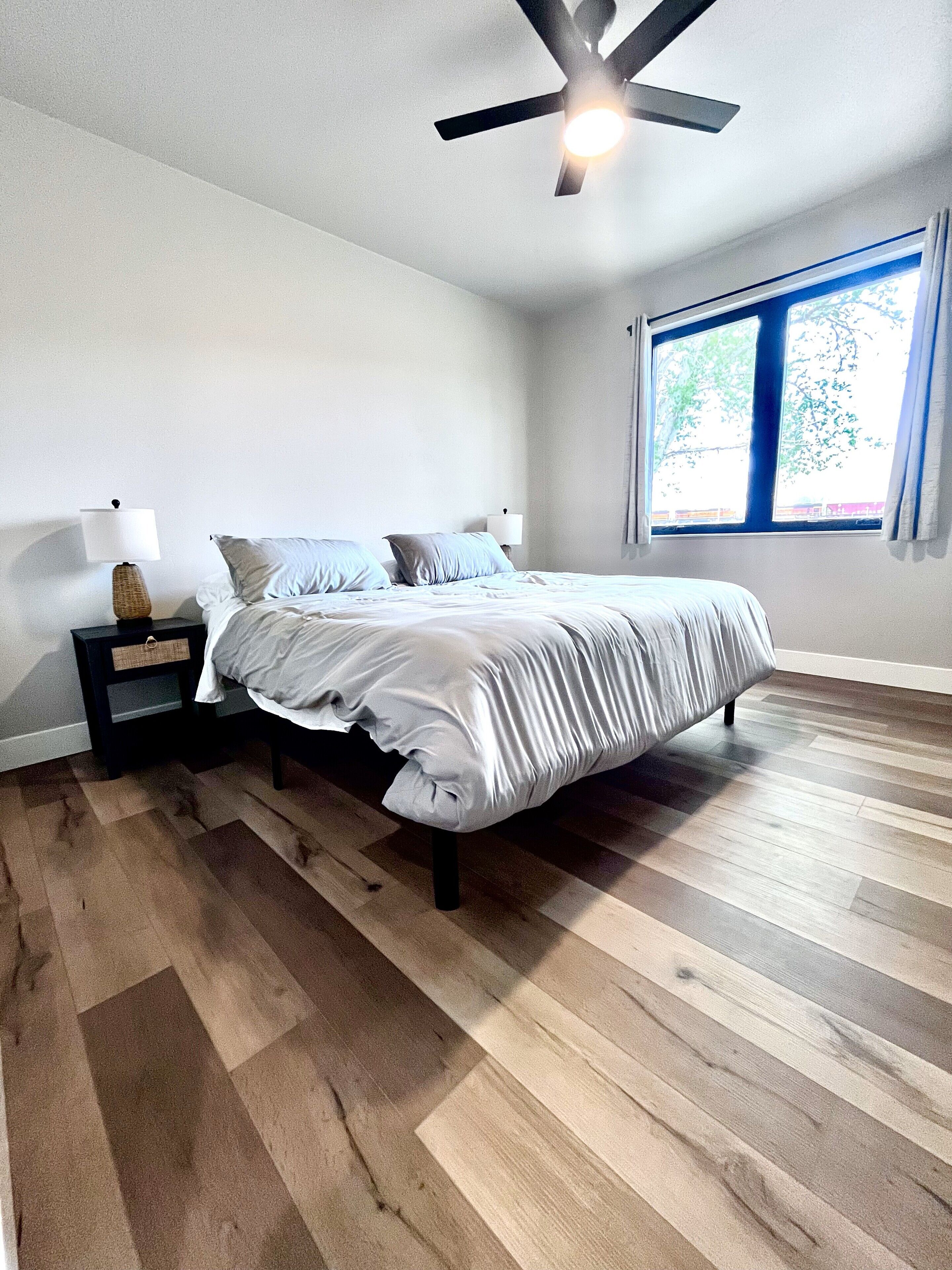 A bedroom with a bed, nightstands, a ceiling fan, and a window with curtains.