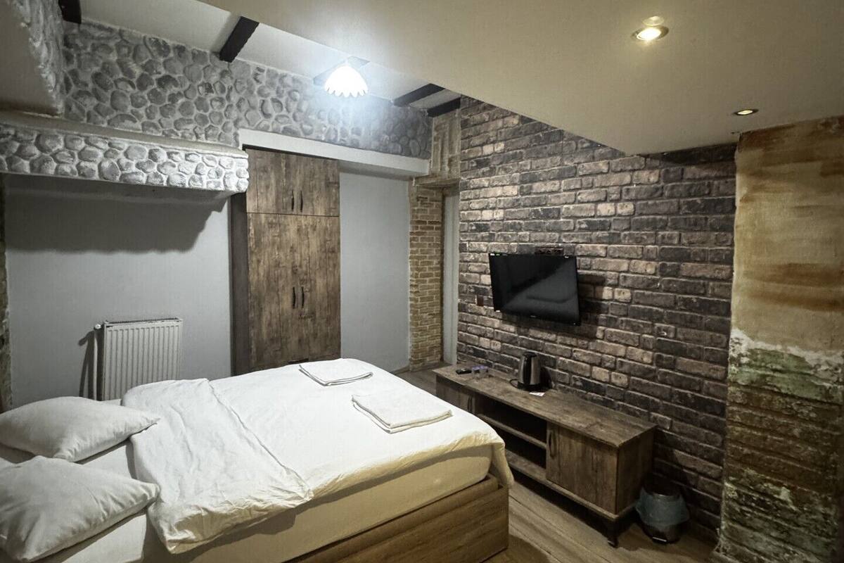 Un dormitorio con cama, televisor montado en una pared de ladrillo, una pared decorativa de piedra y suelo de madera.