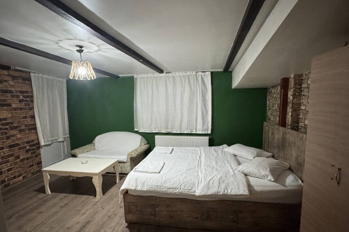 Un dormitorio con cama, una mesita, una silla, una lámpara colgante y una pared de ladrillo.