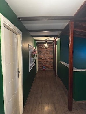 Un couloir aux murs verts, avec un plancher en bois, une porte blanche, un tableau encadré, un mur en briques et un ventilateur de plafond.