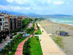 A coastal road with buildings, parked cars, and a beach. - Cağaloglu Apart Butik Otel (Atakum)