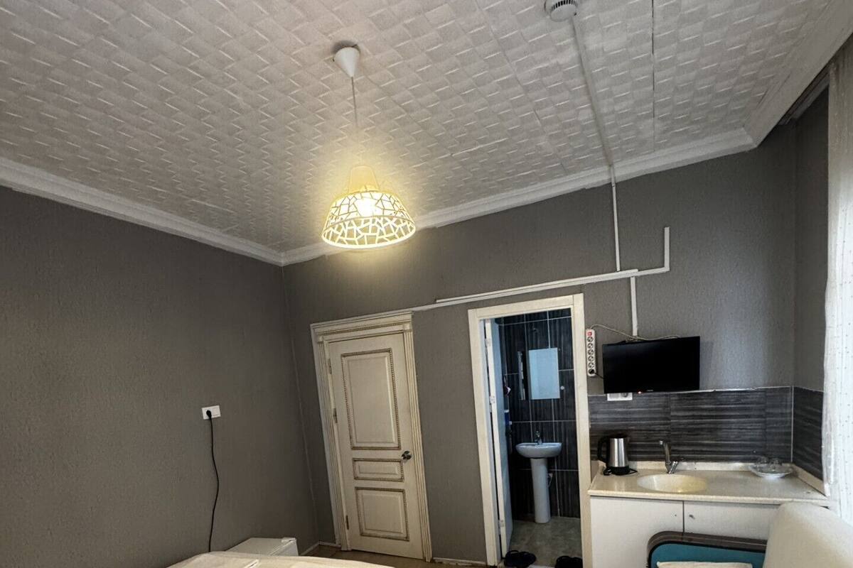 Un dormitorio con cama, mesita de noche, armario, una pequeña cocina americana con lavabo y televisor.