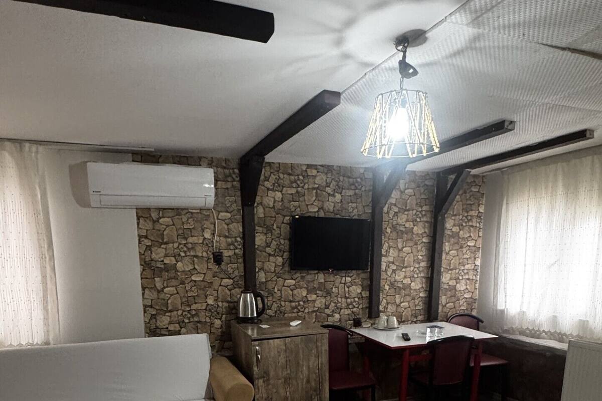 Una habitación con sofá, cama, mesa y sillas, televisor montado en una pared de piedra y un equipo de aire acondicionado.