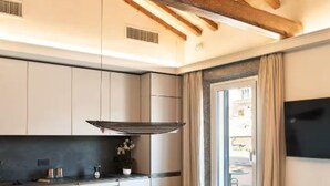 A modern kitchen with wooden beams, a dining table with chairs, and a TV mounted on the wall.