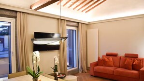 A modern living room with a sofa, a dining table with a vase of flowers, and a TV mounted on the wall.
