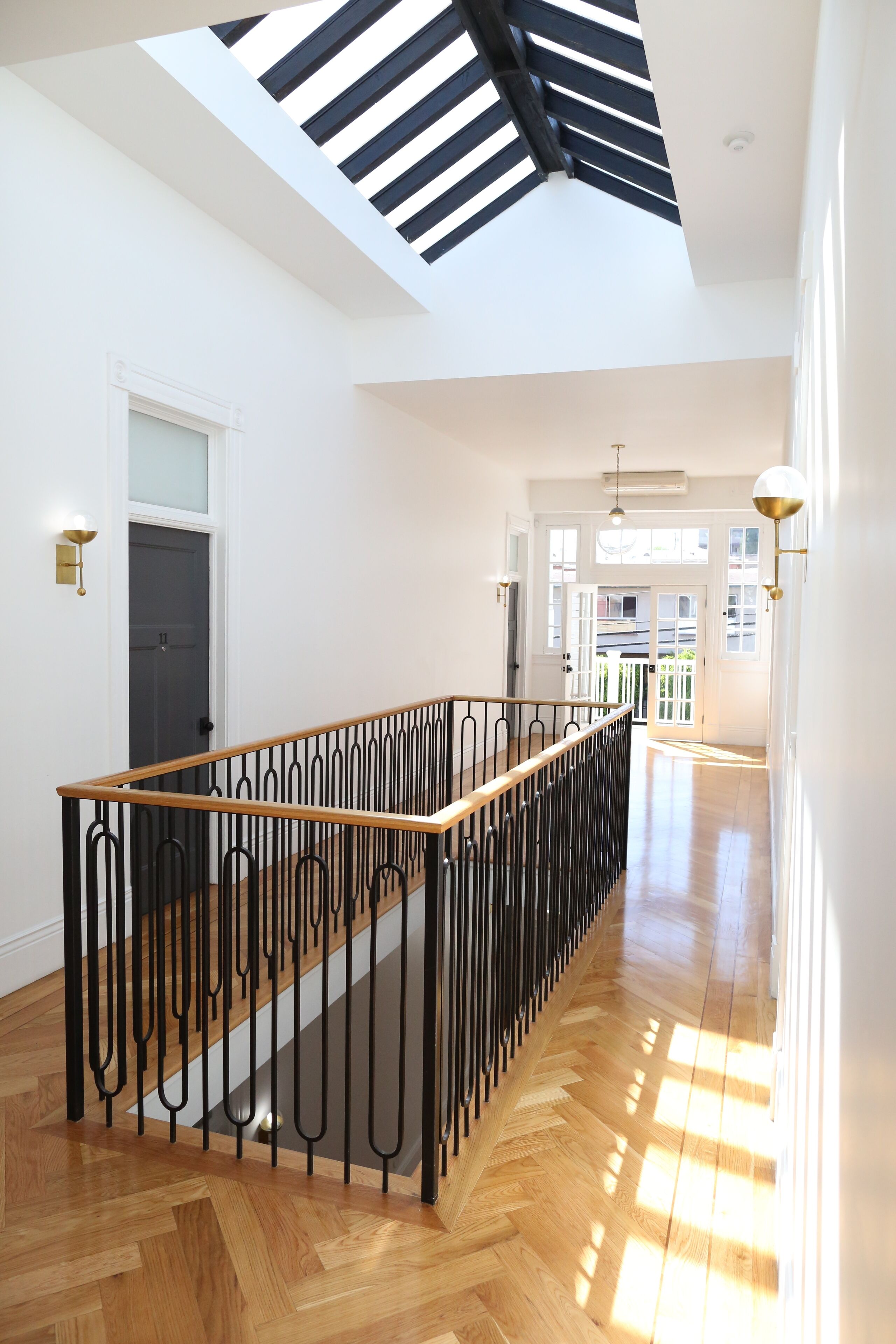 A spacious hallway with a wooden floor, a black metal railing, and a skylight above.