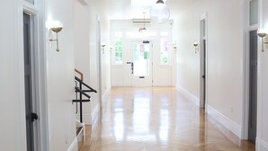 A hallway with wooden flooring, white walls, and a staircase on the left. - The Burlington Hotel (Los Angeles)