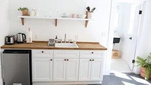 A kitchen with white cabinets, a wooden countertop, a sink, a refrigerator, and a potted plant. - The Burlington Hotel (Los Angeles)