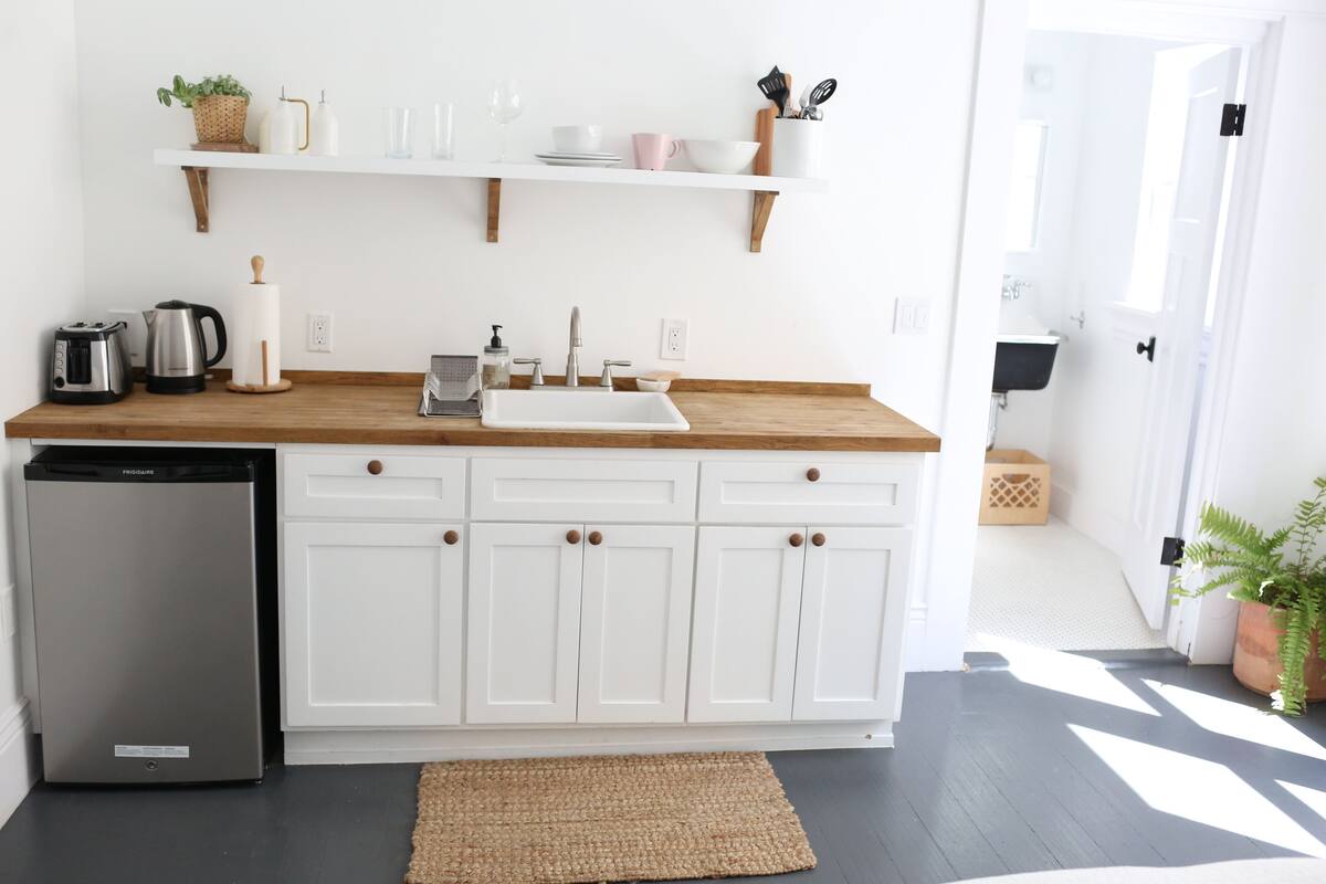 A kitchen with white cabinets, a wooden countertop, a sink, a refrigerator, and a potted plant.