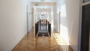 A spacious hallway with wooden flooring, a central staircase, and a dining area with a long table and chairs. - The Burlington Hotel (Los Angeles)