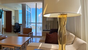 A hotel room with a sofa, a table, a lamp, and a view of the city through large windows. - AKA Hotel Stunning Views w- Free parking (Miami)
