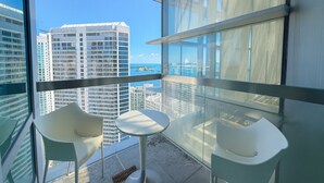 A balcony with two white chairs and a small table, overlooking a cityscape with tall buildings and a view of the ocean. - AKA Hotel Stunning Views w- Free parking (Miami)