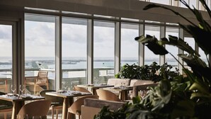 A modern restaurant with large windows offering a view of the water. Tables are set with glasses and cutlery. - AKA Hotel Stunning Views w- Free parking (Miami)