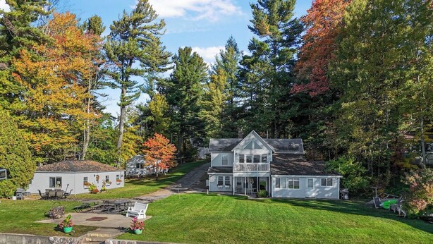 A two-story house with a large front porch, surrounded by a well-maintained lawn and trees with autumn foliage. - Cozy Lakefront 2bd Duplex on Long Lake (Traverse City)