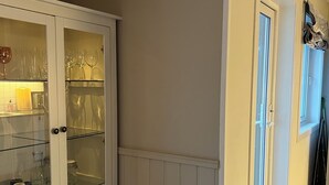 Een keuken met een wit kastje, glazen schappen en een deur naar een andere kamer.