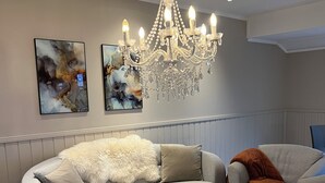 Een moderne woonkamer met een grijze bank, twee ronde salontafels, een kroonluchter en abstracte schilderijen aan de muur.