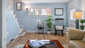 Un salon avec un escalier, une bibliothèque, un fauteuil, une table et une lampe.