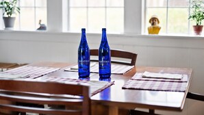 Une table à manger avec deux bouteilles bleues étiquetées « Saratoga » et une nappe à carreaux.