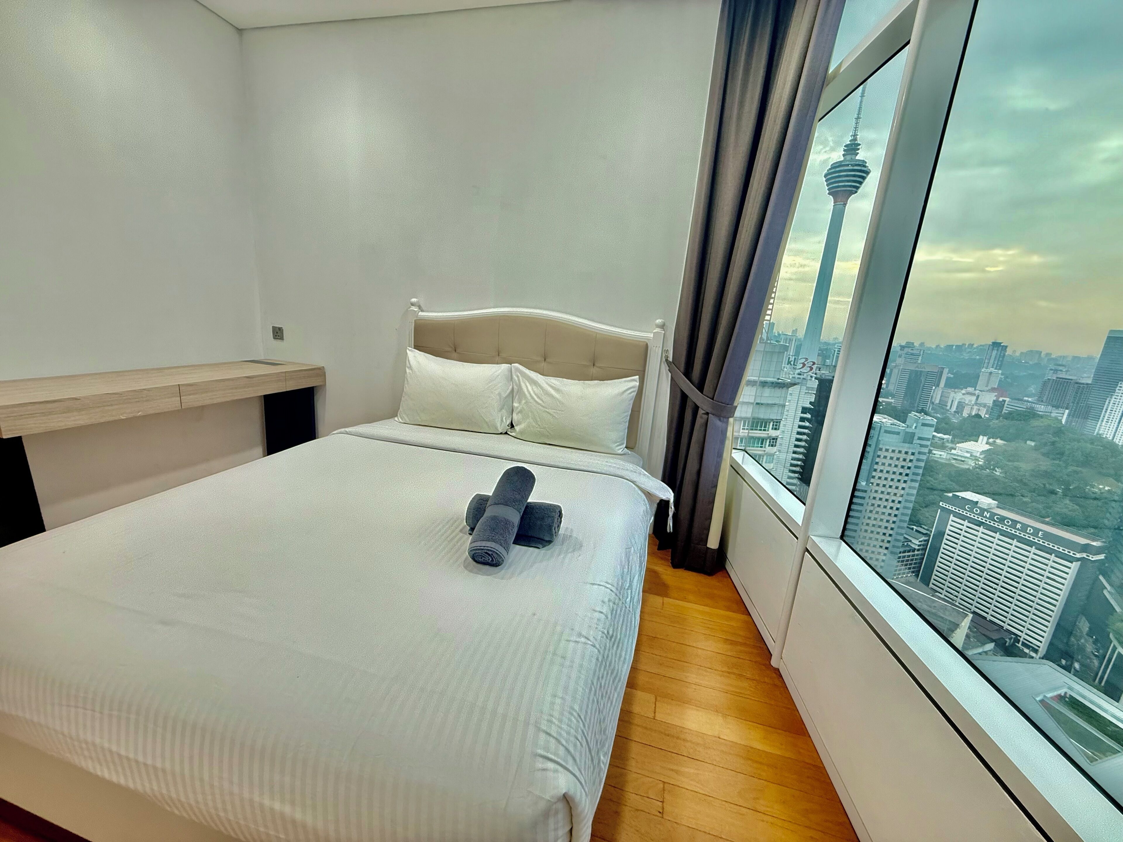 A hotel room with a bed, a wooden nightstand, and a large window offering a city view.