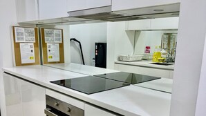 A modern kitchen with white cabinetry, a black induction cooktop, a built-in oven, and a stainless steel range hood. There are two bulletin boards on the wall with safety information. - Sky premium suites klcc (Kuala Lumpur)