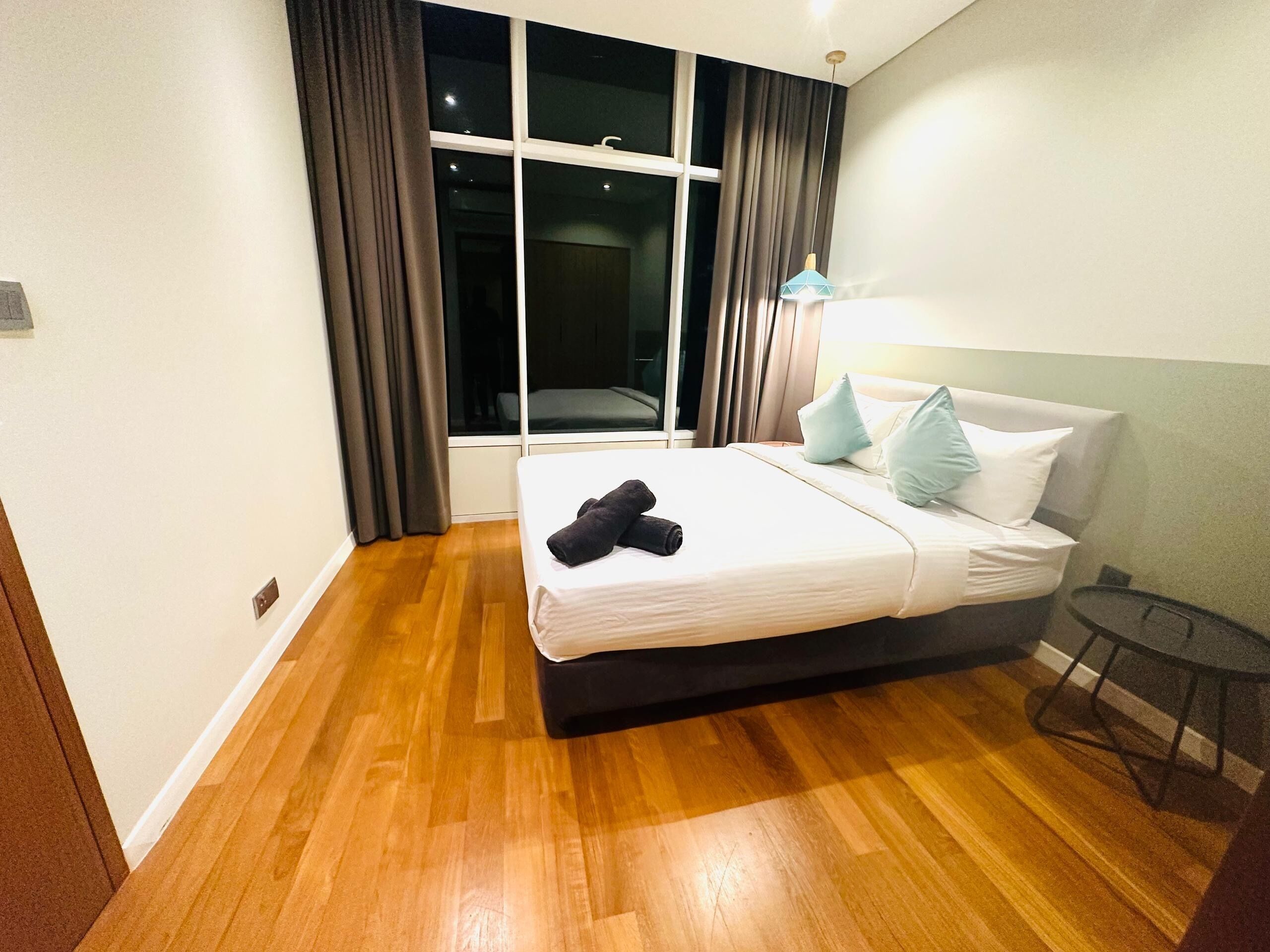 A hotel room with a large bed, a window with curtains, a bedside table, and a lamp.