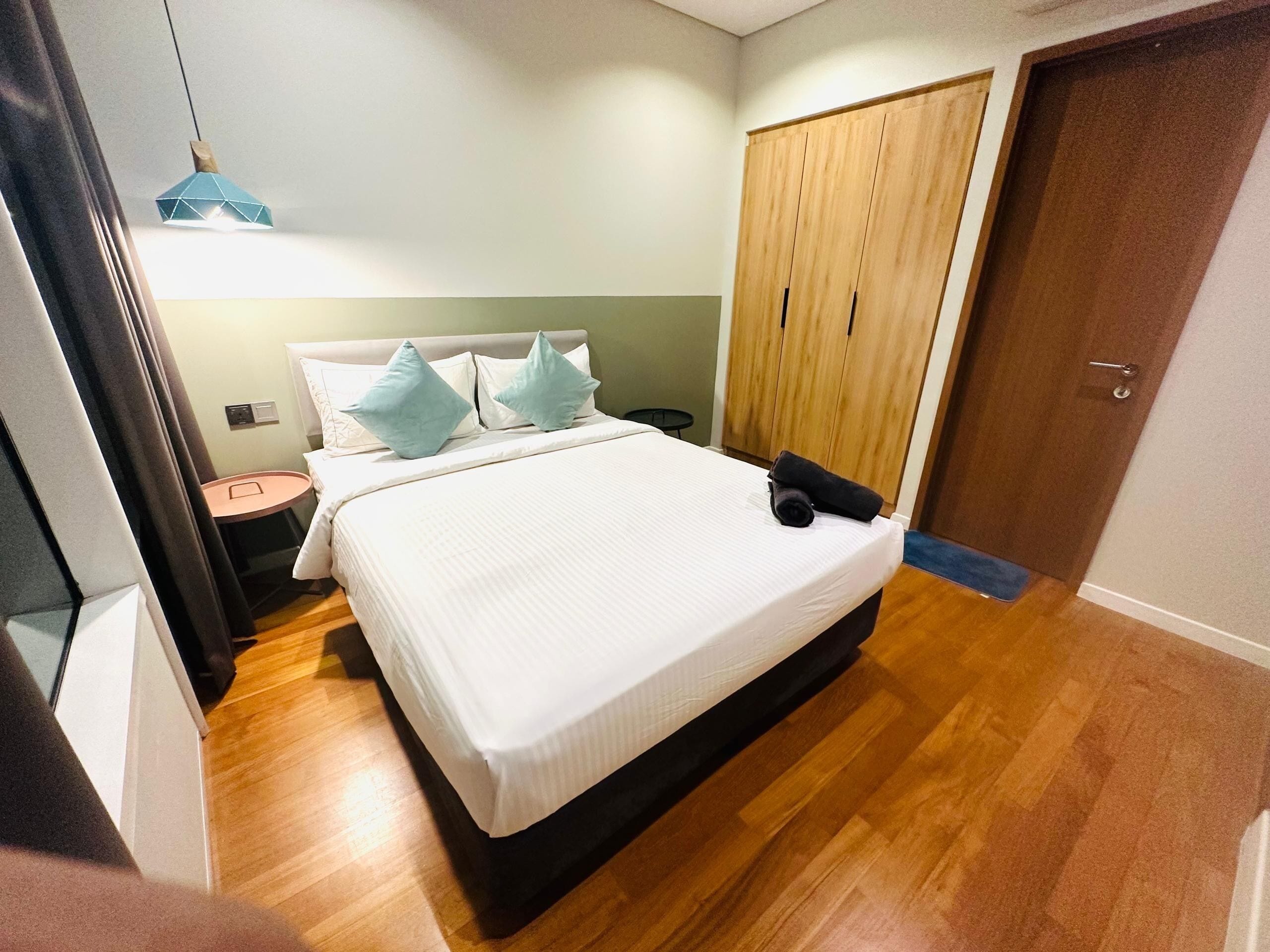 A bedroom with a bed, a wooden wardrobe, a nightstand, and a hanging light fixture.