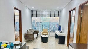 A modern office space with a large window offering a city view, a sofa, a round table, and a desk with a computer. - Sky premium suites klcc (Kuala Lumpur)