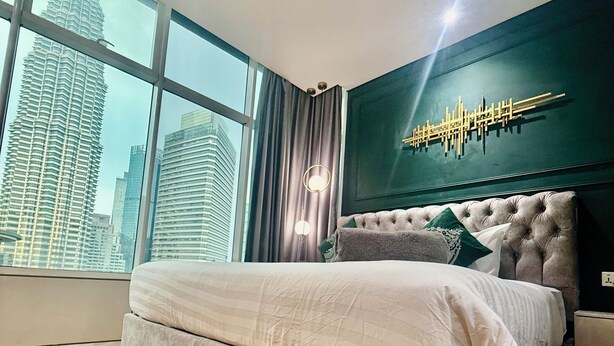 A modern bedroom with a large bed, a city view, and a decorative wall piece. - Sky premium suites klcc (Kuala Lumpur)