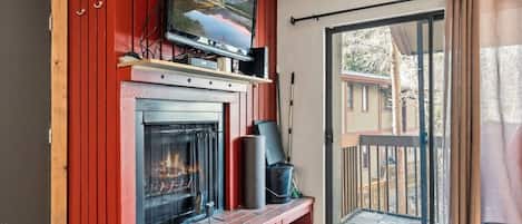 A cozy room with a fireplace, a television mounted above it, and a sliding glass door leading to an outdoor deck.