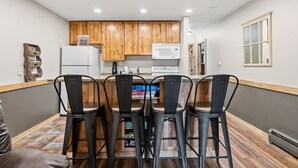A modern kitchen with wooden cabinets, a white refrigerator, a microwave, and a dining area with four chairs. - Mountain Charmer | Steps to Main St & Trails (Frisco)